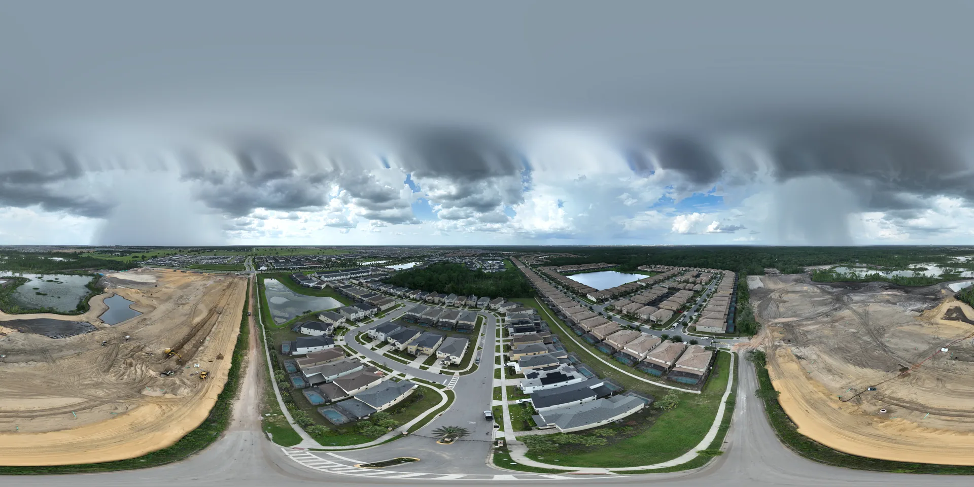 Equirectangular aerial panorama of a master-planned residential community under active expansion in Central Florida. The panoramic view shows completed single-family homes with landscaped yards and paved streets in the center, flanked by active earthwork and grading operations on both sides where new home sites are being prepared. Retention ponds, wetland areas, and forested perimeter are visible across the development. Captured from a commercial drone platform as part of a contract aerial documentation engagement.